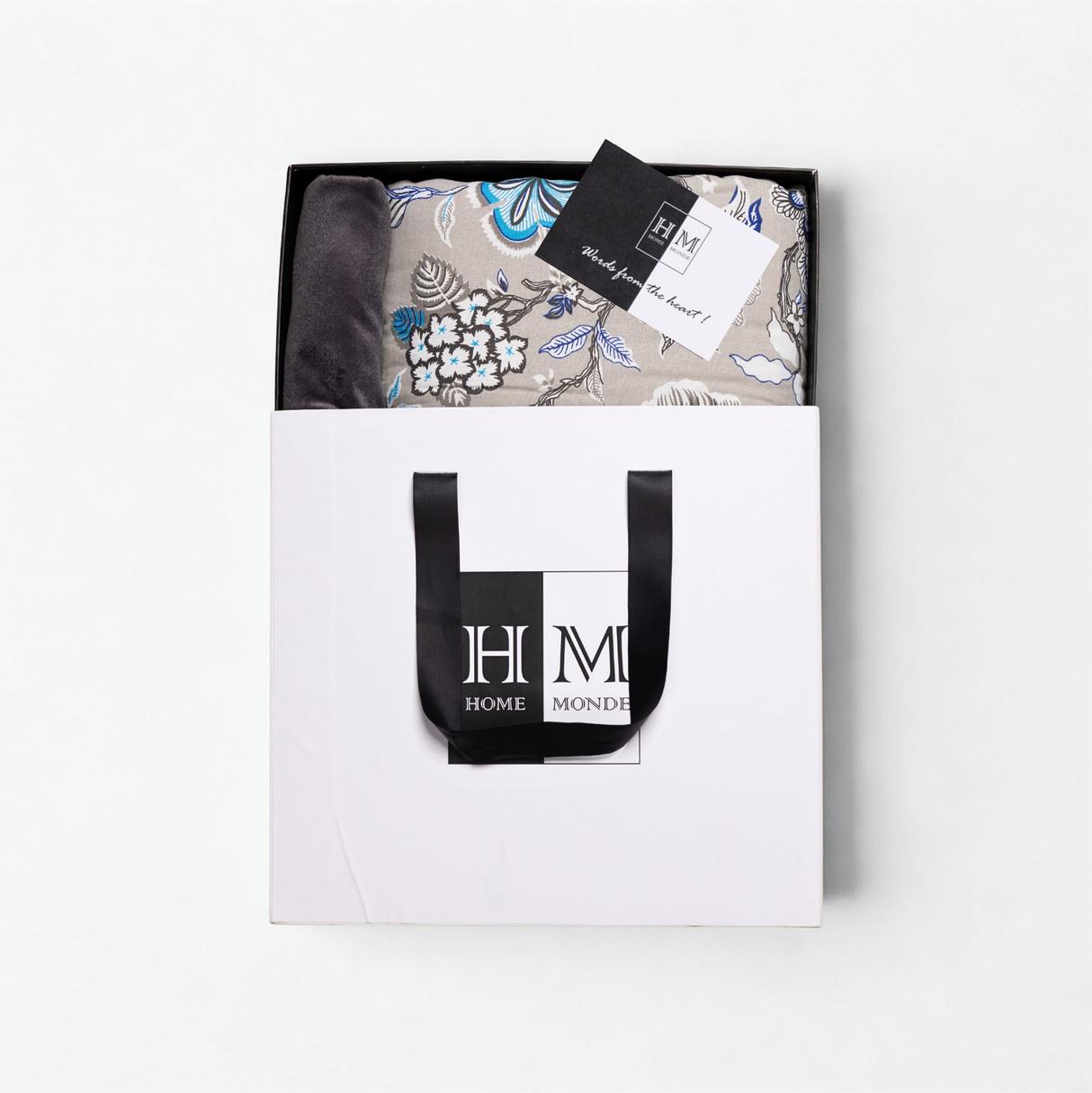 A folded Premium Dohar & Cushion Cover Combo Set in a white gift bag with black handles and the HOME MONDE logo, plus a 锟斤拷锟組ade from the heart锟斤拷锟 tag锟斤拷锟絠deal for gifting or as a stylish hom