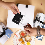 Two hands exchange a card reading 锟斤拷锟紿M, Work from the heart!锟斤拷锟 in front of a Premium Bedsheet & Cushion Covers Combo Set arranged in a gift-ready box with assorted sweets and fabric accents on a be